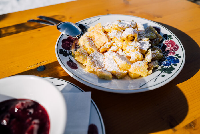 Kaiserschmarrn with icing sugar on a plate with flowers around the edge | © Chris Perkles_SalzburgerLandTourismus_www.filzmoos.at