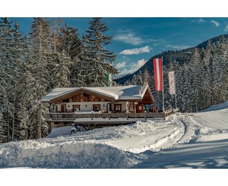 Skihütte neben einer Piste und dahinter sind schneebedeckte Bäume