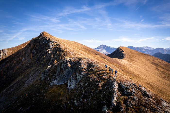Four hikers are walking to the summit of the Großarler Gründegg and are photographed from above by a drone. | © Gipfelfieber
