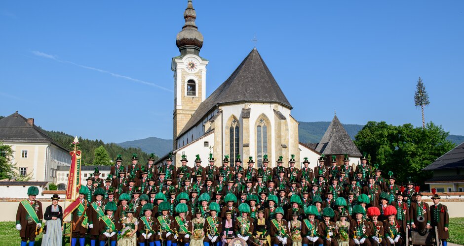 The Struckerschützen Altenmarkt in costume with flag and cannon pose in front of the church in morning sunlight | © Struckerschützen Altenmarkt