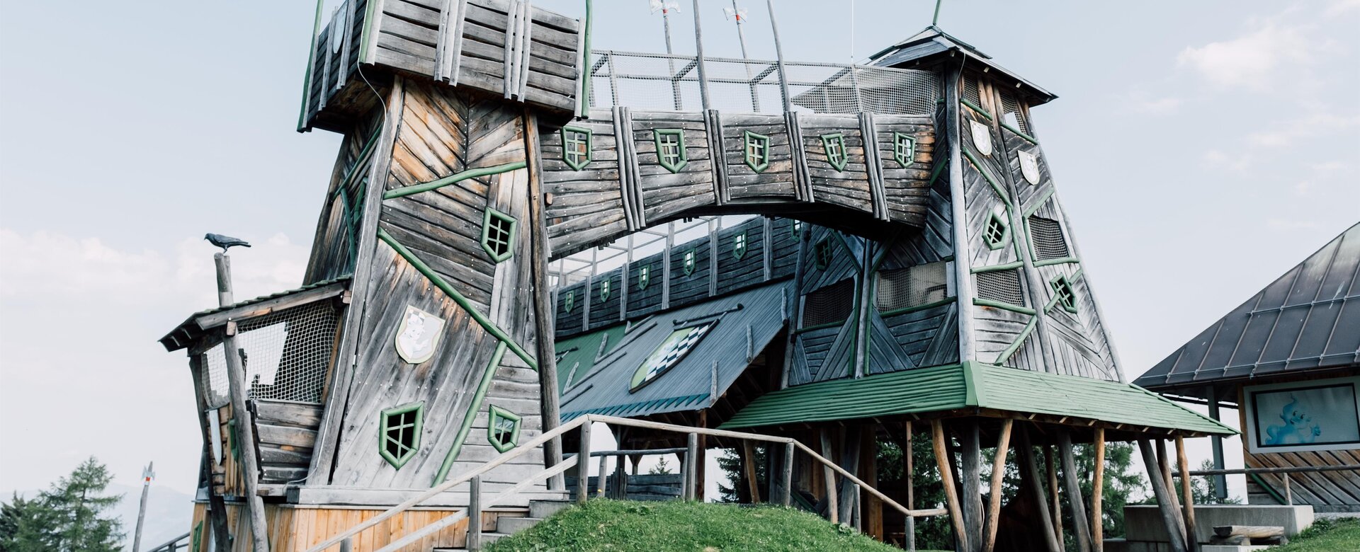 Tilted wooden fortress with bridge and turrets at Geisterberg, green shutters and red flag fluttering | © JOSalzburg
