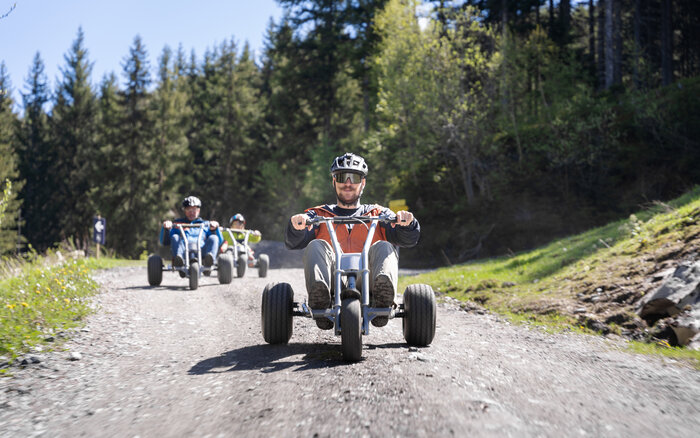 Gruppe fährt mit Mountaincarts rasant bergab auf Schotterweg durch Waldgebie | © Dorfgasteiner Bergbahnen AG
