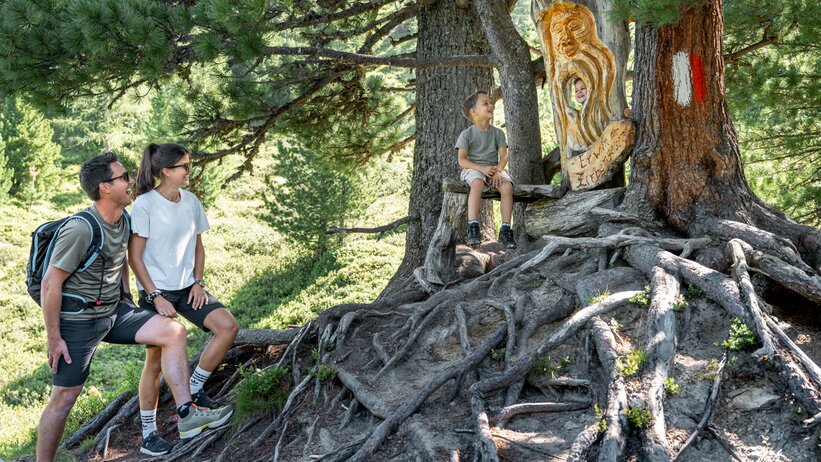 Family at Graukogel by carved pine spirit on a root bench in the forest | © Skigastein, seven frames