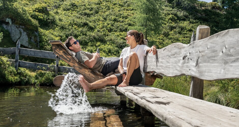 Couple relaxing on wooden loungers with feet in mountain water at Graukogel | © Skigastein, seven frames