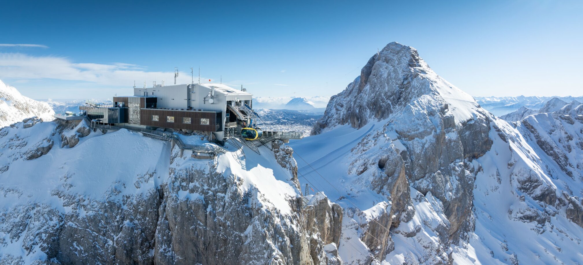 A modern mountain station with a cable car on a snow-covered peak, surrounded by an impressive mountain landscape. | © Josh Absenger