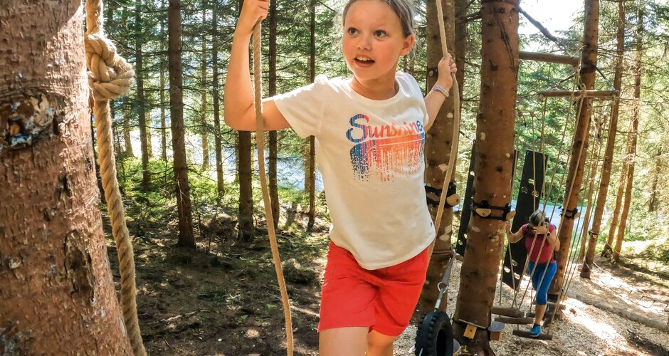 Girl balances on tires in a forest rope course, more kids climbing in the background. | © Shuttleberg