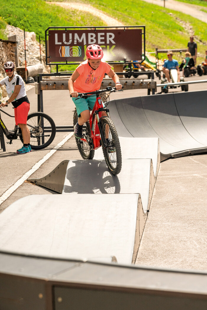 Child rides red mountain bike with helmet and pink shirt on pump track bumps | © Shuttleberg