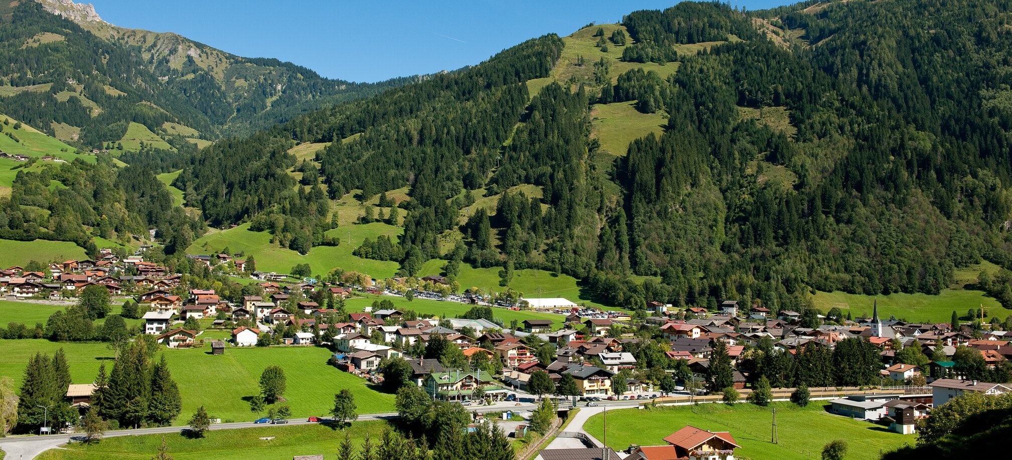 Dorfgastein in summer with traditional houses and green meadows beneath forested Alpine slopes | © Fotoatelier Wolkersdorfer