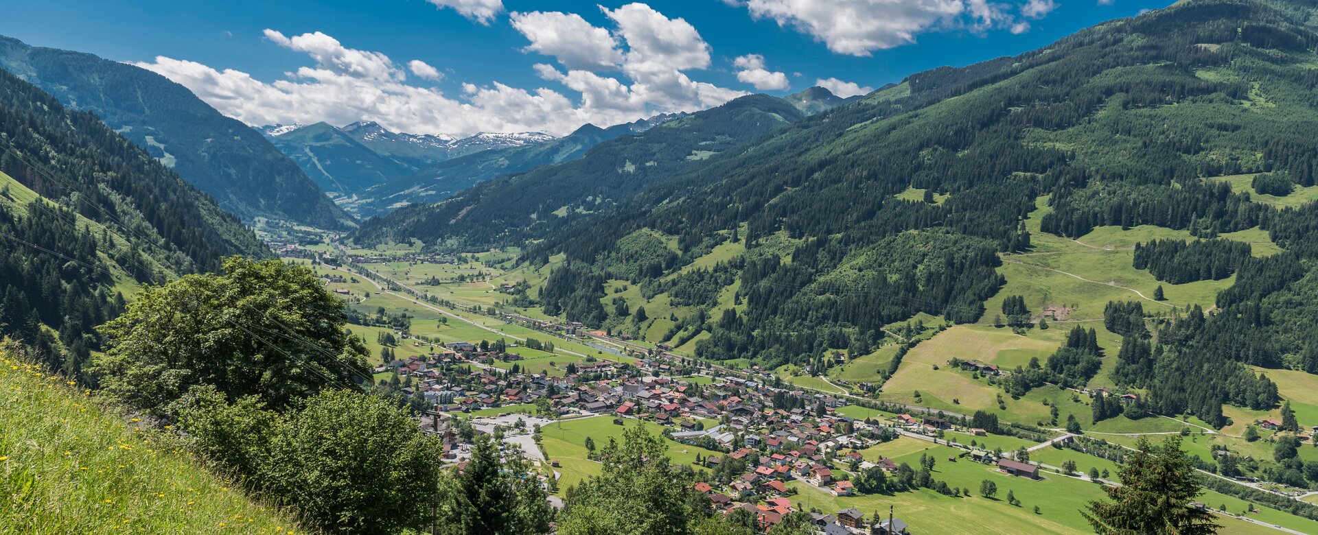 Wide view of Dorfgastein with green meadows, forested mountains and Gastein Valley under blue sky | © Gasteinertal Tourismus GmbH