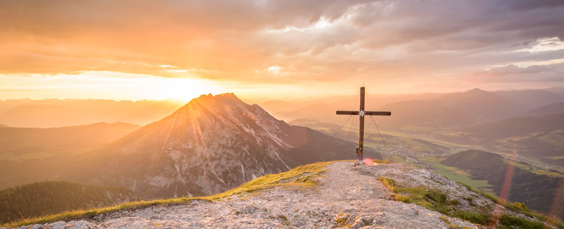 Summit cross at sunrise overlooking Gröbming area, mountain scenery bathed in golden morning light | © Christoph Huber