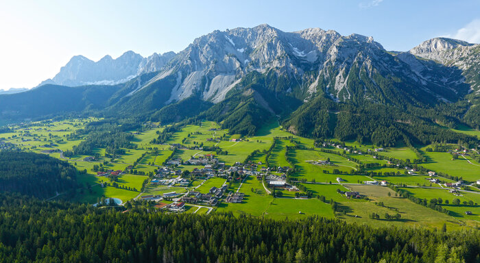 Aerial view of the Ramsau plateau with wide green meadows, scattered houses and the mighty Dachstein mountain backdrop | © Herbert Raffalt
