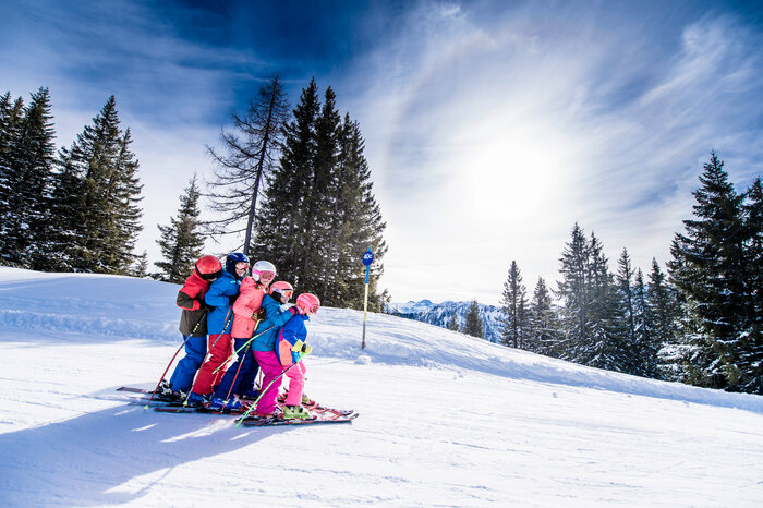 Six children in colorful ski outfits ski closely together down the slope, smiling and enjoying the snow.