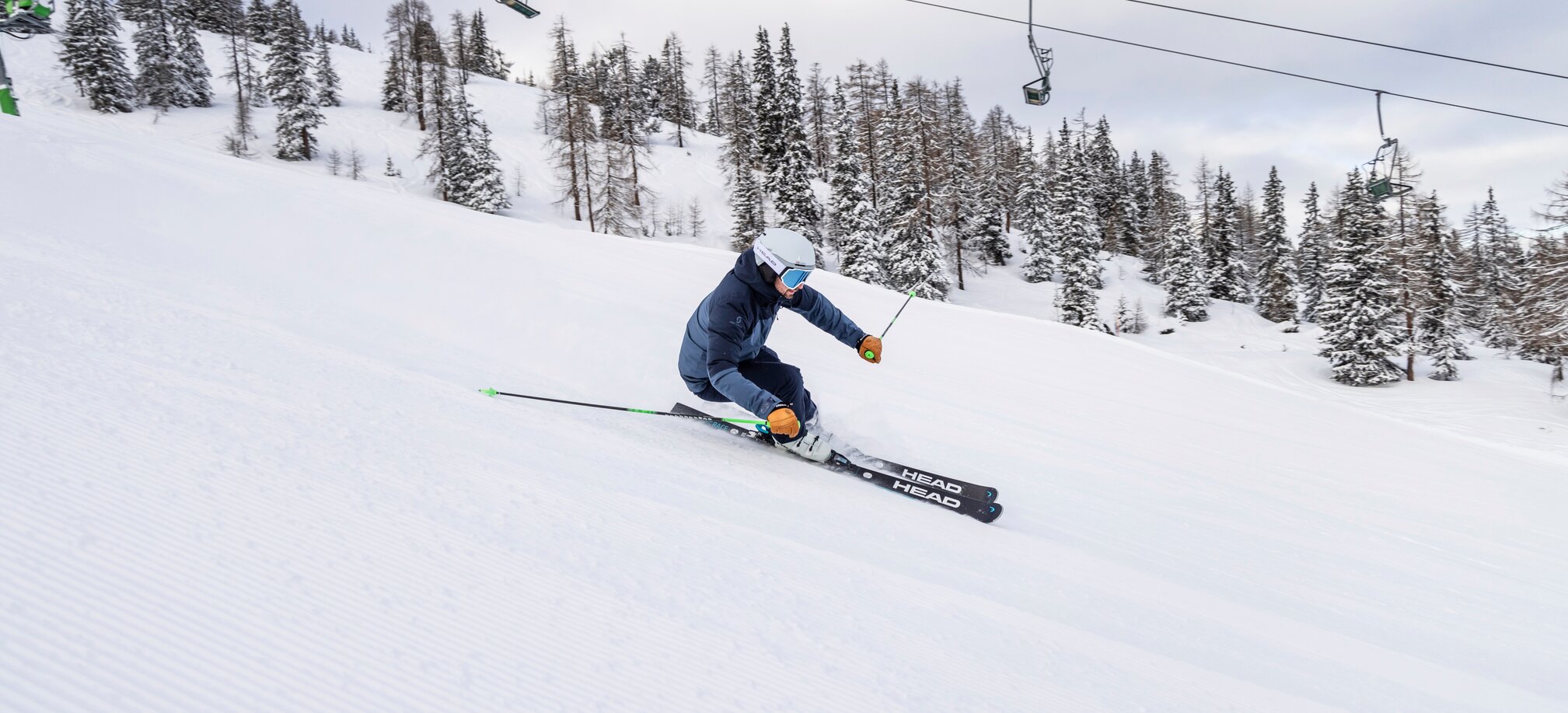 Skier descending a freshly groomed slope with ski lift in the background. | © Mirjah Geh