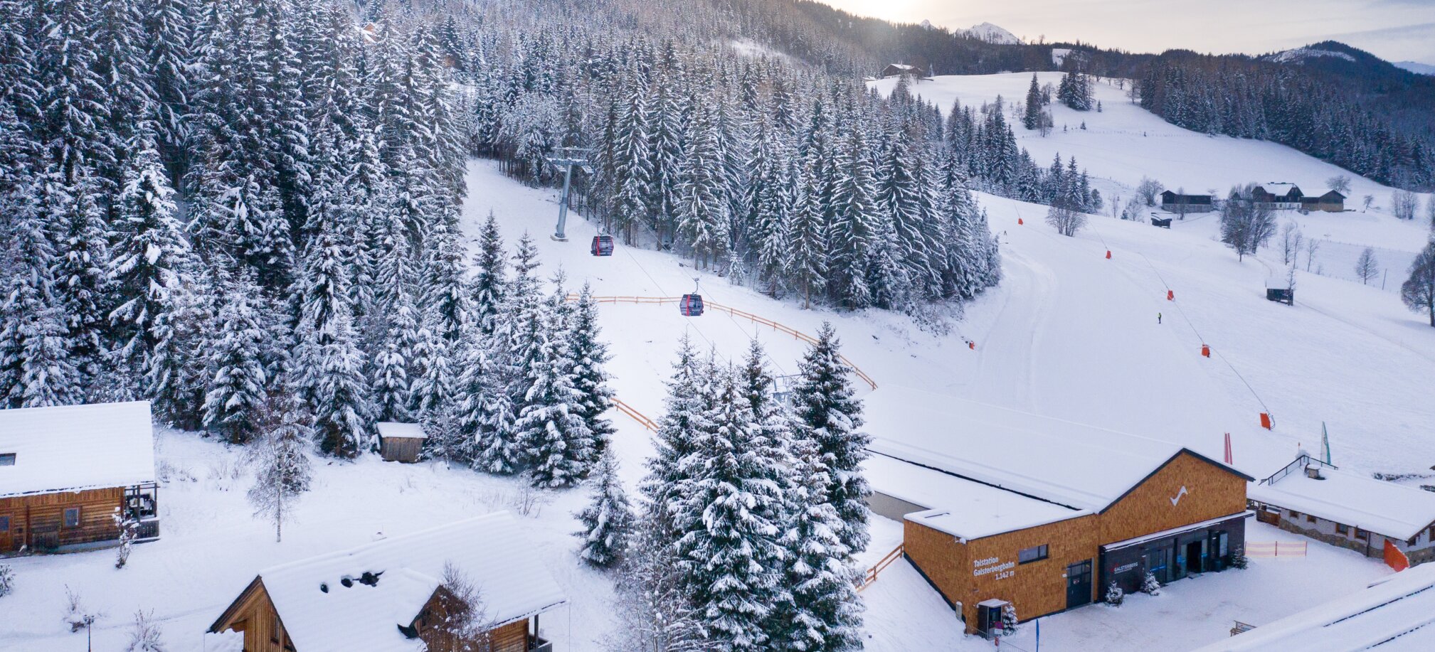 Snowy landscape with gondola valley station and red cabins at Galsterberg. | © Josh Absenger