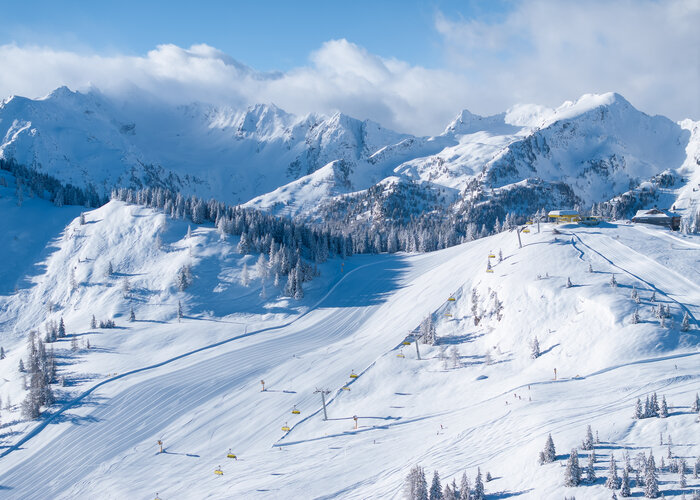 Snowy slopes with chairlifts and majestic alpine backdrop and blue sky. | © Josh Absenger