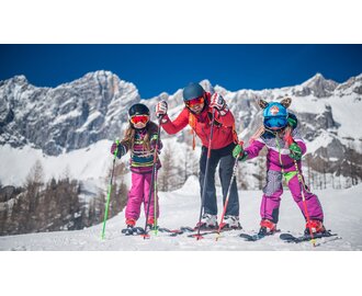 Family with two children skiing in front of a snow-covered mountain backdrop. | © Christine Höflehner