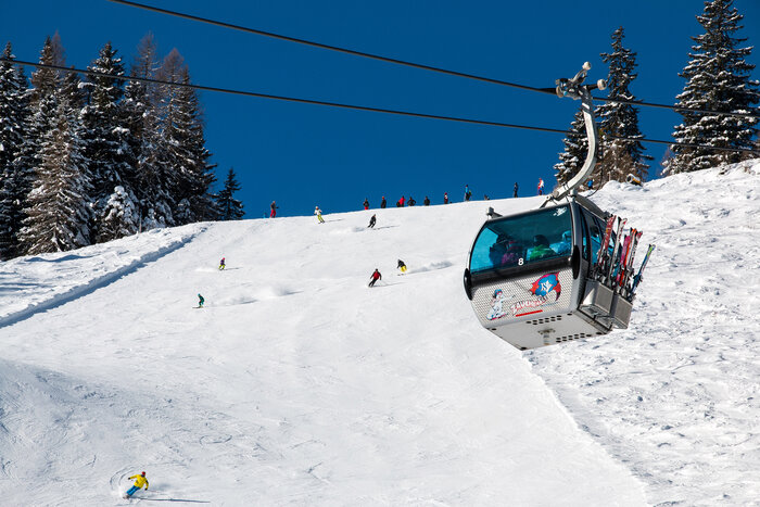 Skiers and gondola at Rosskopfbahn in Zauchensee, snowy slope and forest