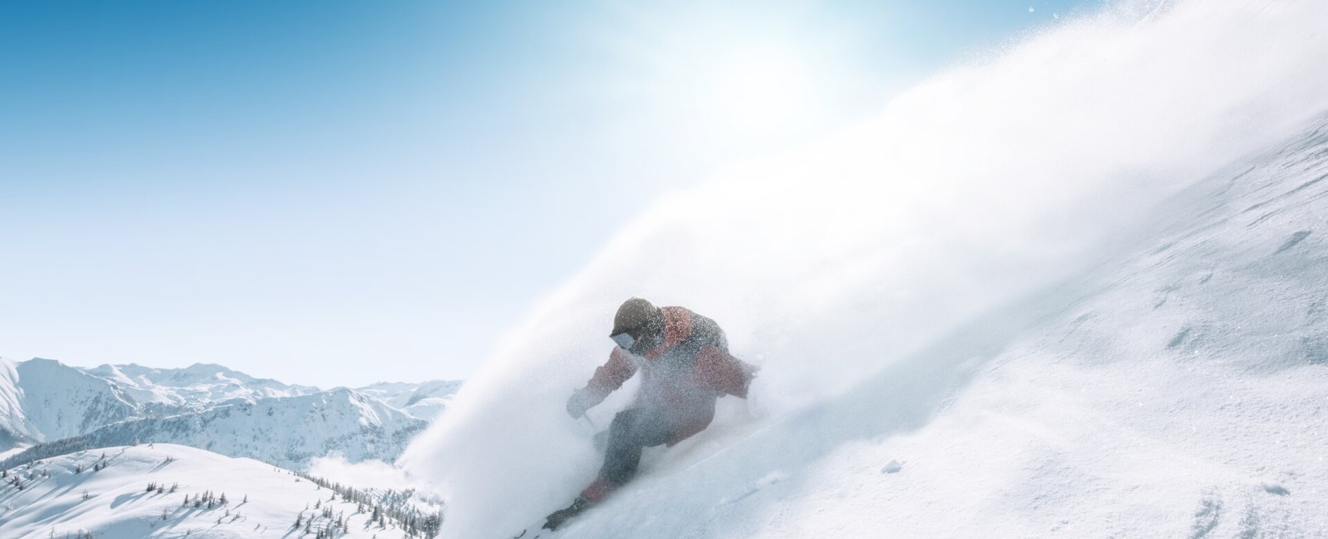 Snowboarder rides down steep slope in deep powder snow, spray clouds in the sunlight
