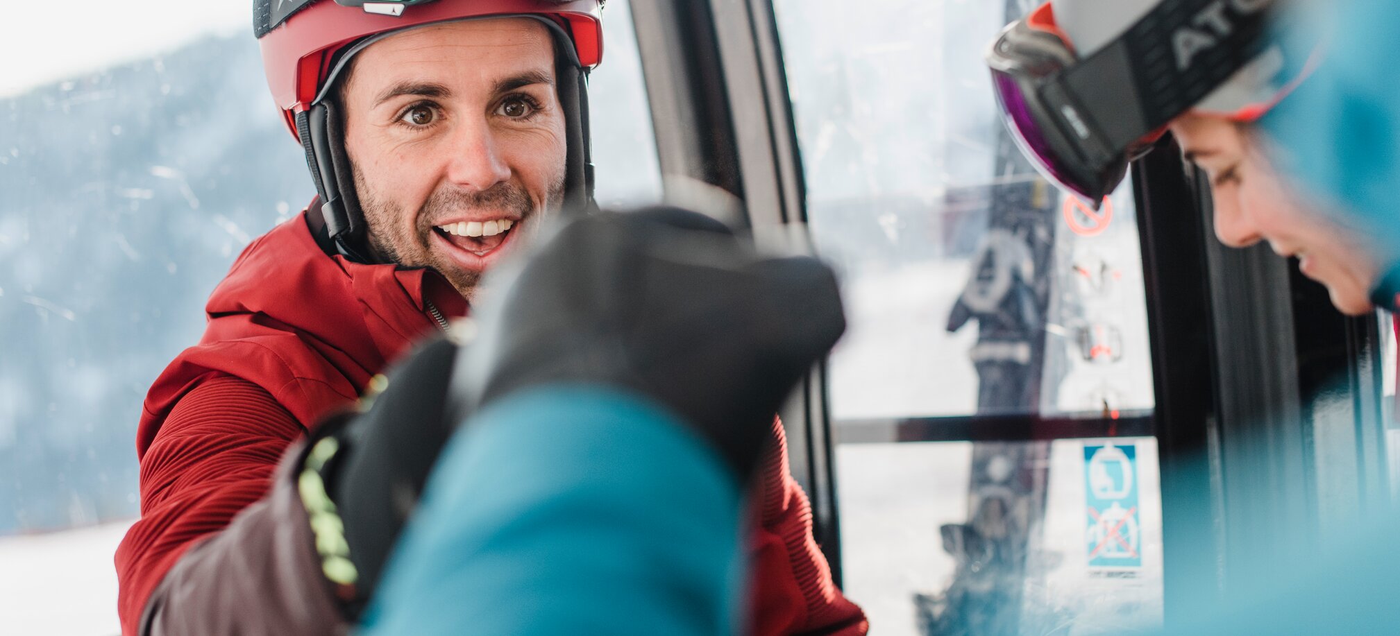 A skier in red clothing gives a friend a fist bump inside the cable car. | © Ski amadé