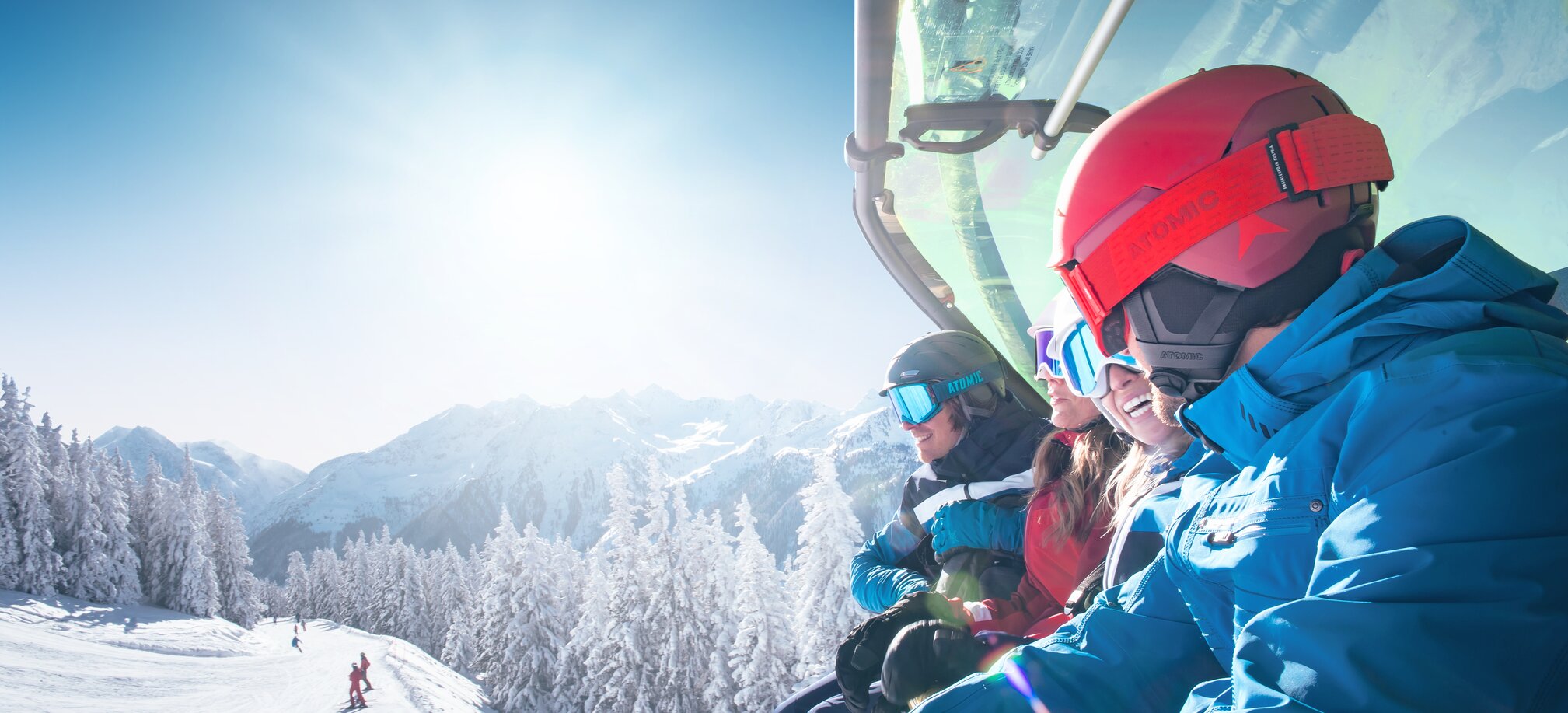 Group of skiers wearing helmets and goggles rides a chairlift with weather cover over a snow-covered mountain landscape. | © Ski amadé