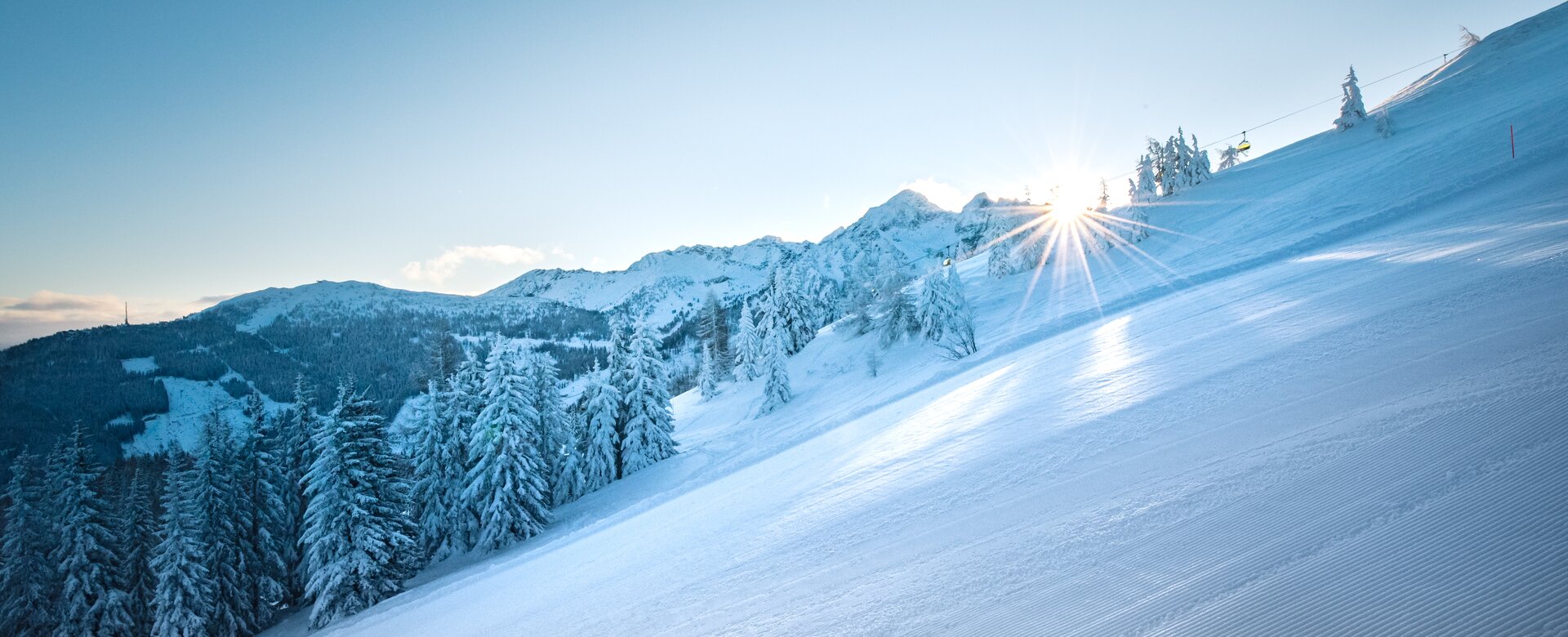 Shining sun over a groomed ski slope with snow-covered trees. | © Ski amadé