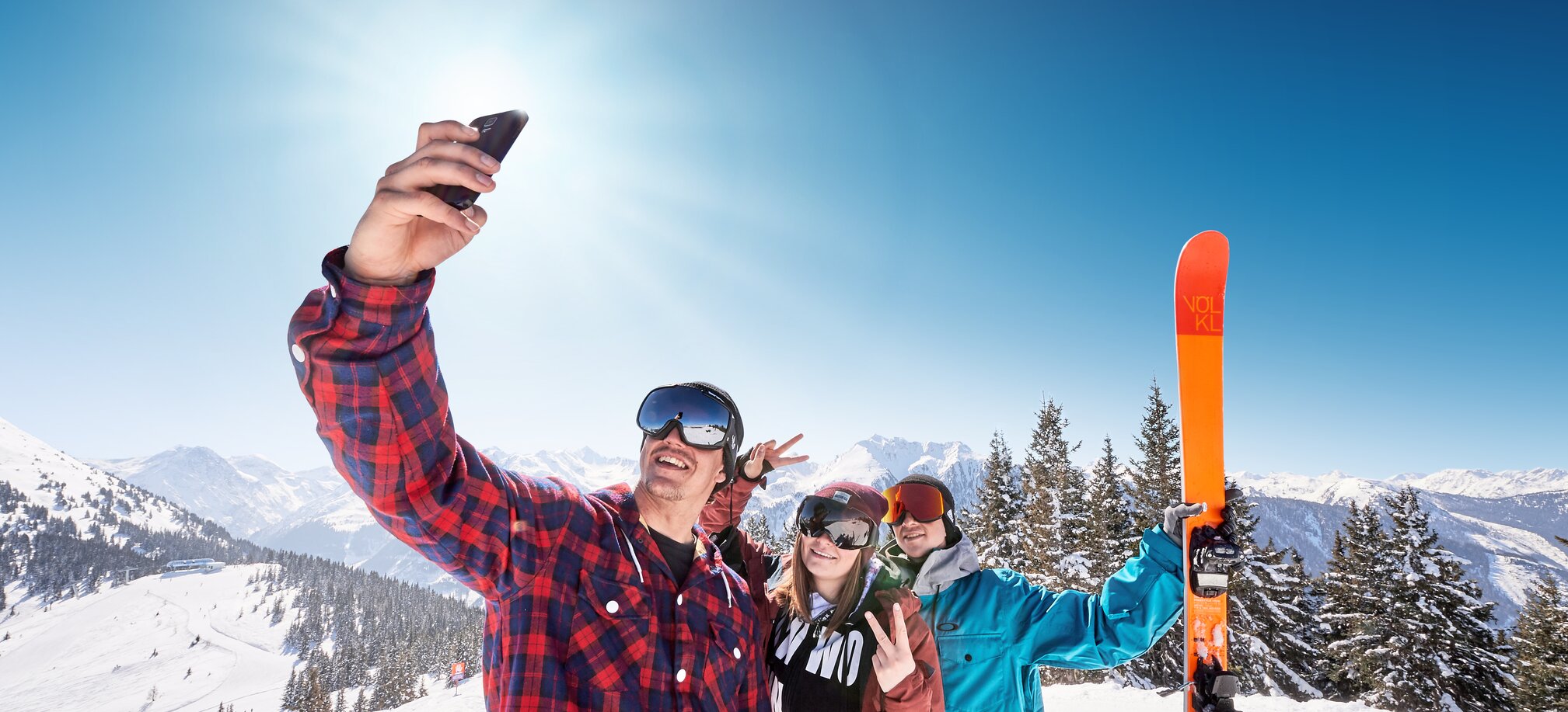 Three youthful skiers pose for a selfie in front of a snow-covered mountain landscape. | © Ski amadé
