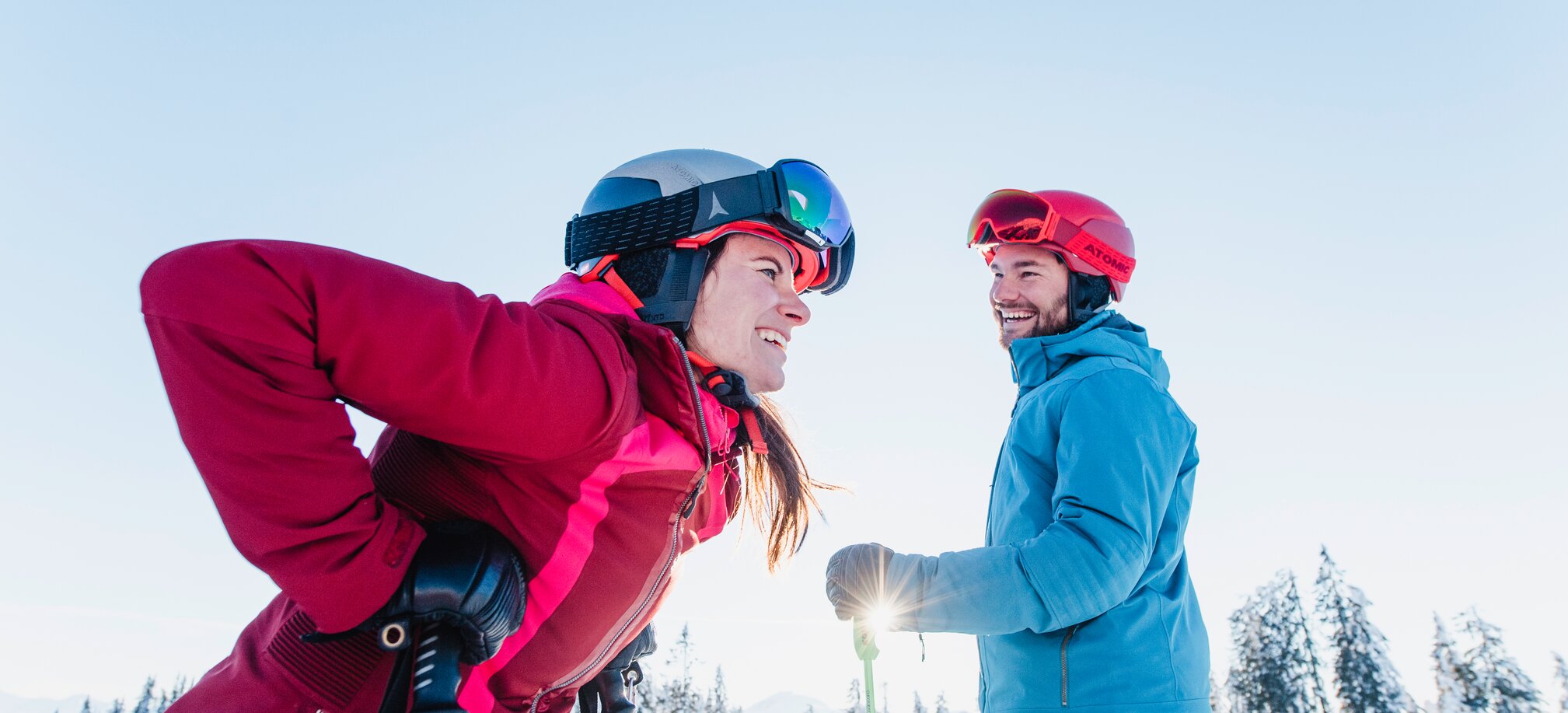 A female skier laughs and leans forward, while a male skier looks at her. | © Ski amadé