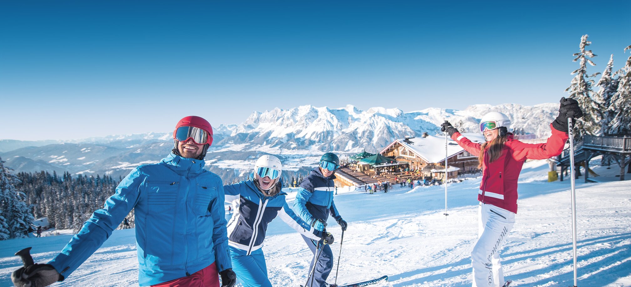 Four skiers laugh on the slope with a mountain hut in the background. | © Ski amadé