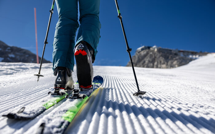 Nahaufnahme eines Tourenskischuhs auf gespurer Piste mit Stöcken und Sonne im Hintergrund | © Harald Steiner