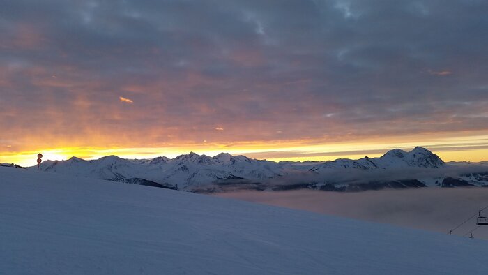 Snow-covered slopes with orange sunrise and clouds above mid-station in the mountains