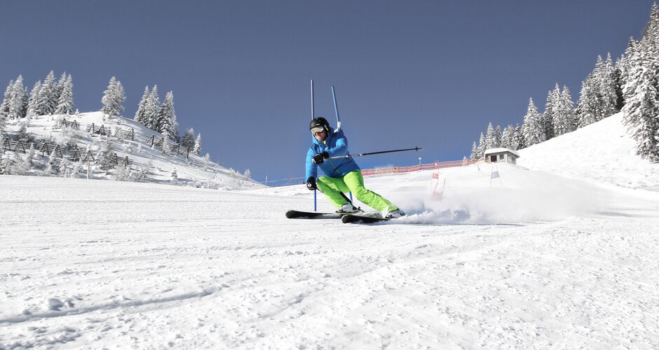 A skier in green pants slaloms through blue gates on a sunny slope in Alpendorf Pongau